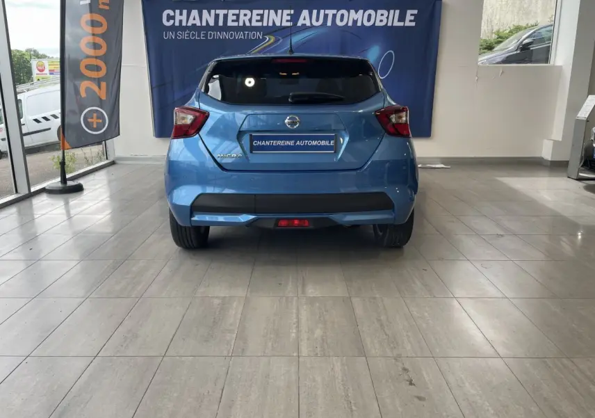 Vue arrière d'une Nissan Micra bleu vif en showroom, avec logo et feux arrière distinctifs bien visibles.