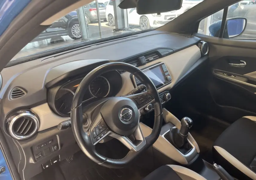 Vue intérieure côté conducteur de la Nissan Micra bleu 2020, volant cuir multifonctions et écran tactile central visible.