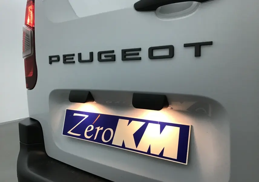 Gros plan arrière gauche du Peugeot Partner blanc 2025 avec plaque d'immatriculation éclairée "Zéro KM" visible.