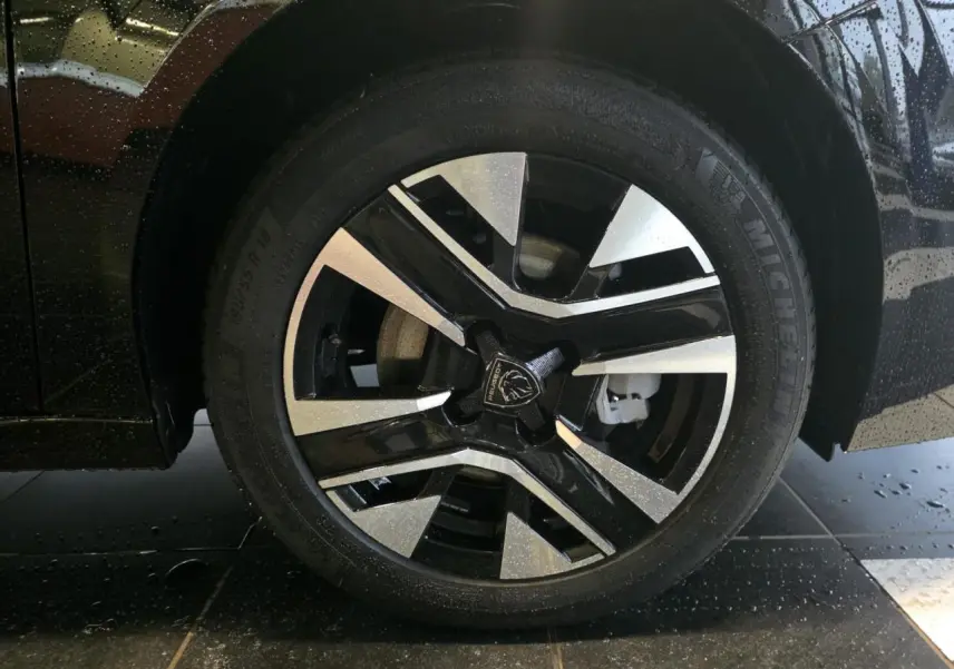 Gros plan sur la jante alliage 16'' bi-tons noir et argentée de la Peugeot 208 noire métallisée, roue avant droite.