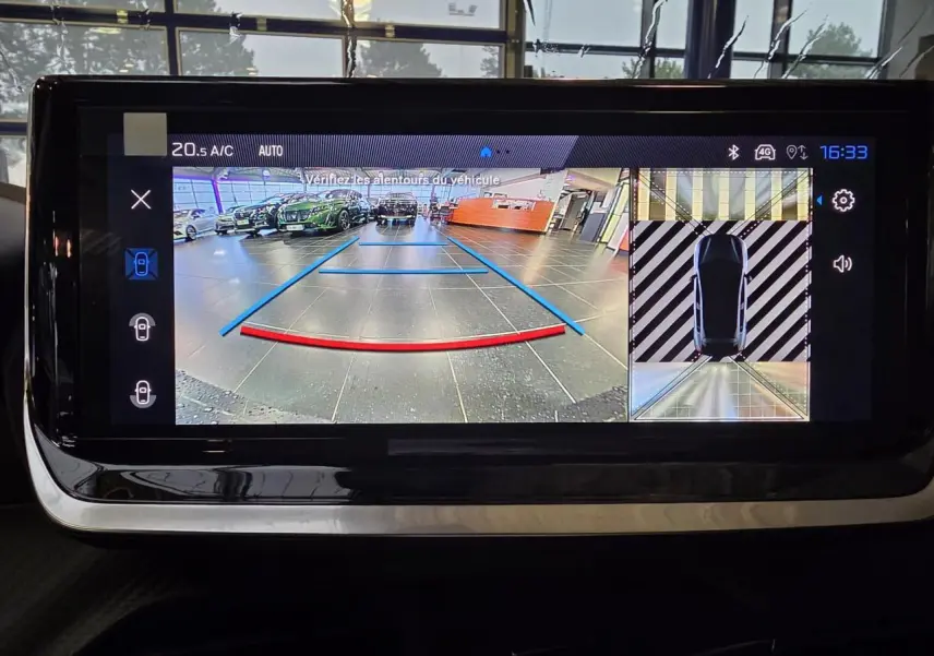 Écran tactile affichant la caméra de recul et vue 360° d’une Peugeot 208 noire métallisée en stationnement intérieur.