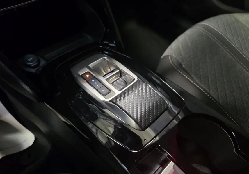 Vue rapprochée de la console centrale noire brillante avec levier de boîte automatique et sellerie tissu gris Peugeot 208 hybride 2025.