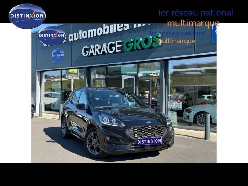 Ford Kuga 2024 noir Agate métallisé en 3/4 avant, avec calandre hexagonale et jantes alu sombres, devant un garage multimarque.