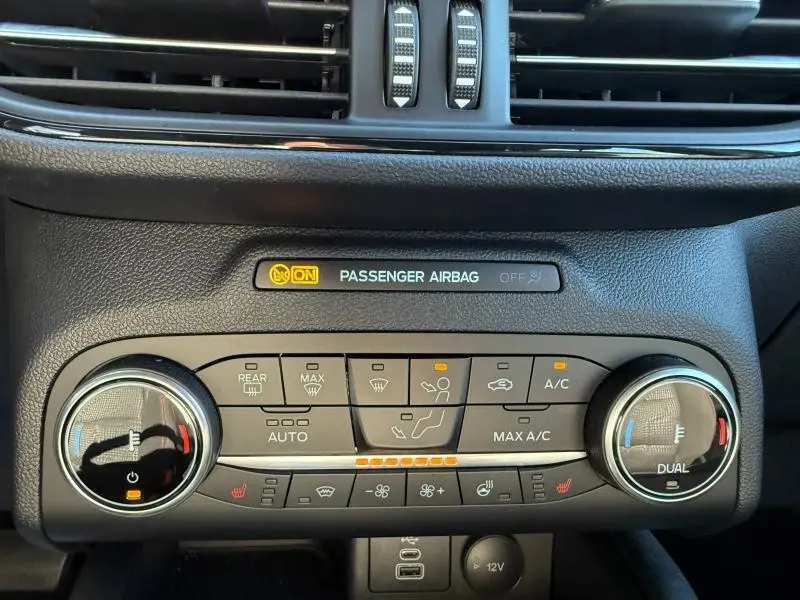 Vue rapprochée du tableau de bord du Ford Kuga 2024 noir, montrant la commande de climatisation bi-zone et l'indicateur airbag passager.
