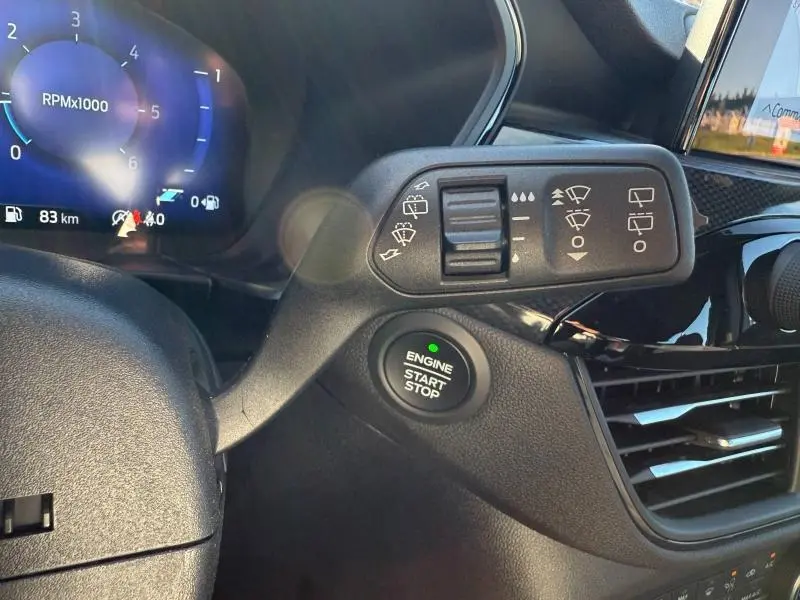 Gros plan intérieur sur le volant et la commande des essuie-glaces du Ford Kuga noir avec bouton start/stop et tableau de bord numérique.