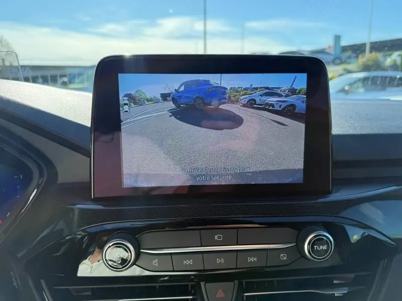 Vue écran caméra de recul montrant un Ford Kuga 2.0 EcoBlue noir Agate métallisé en 3/4 arrière sur parking.