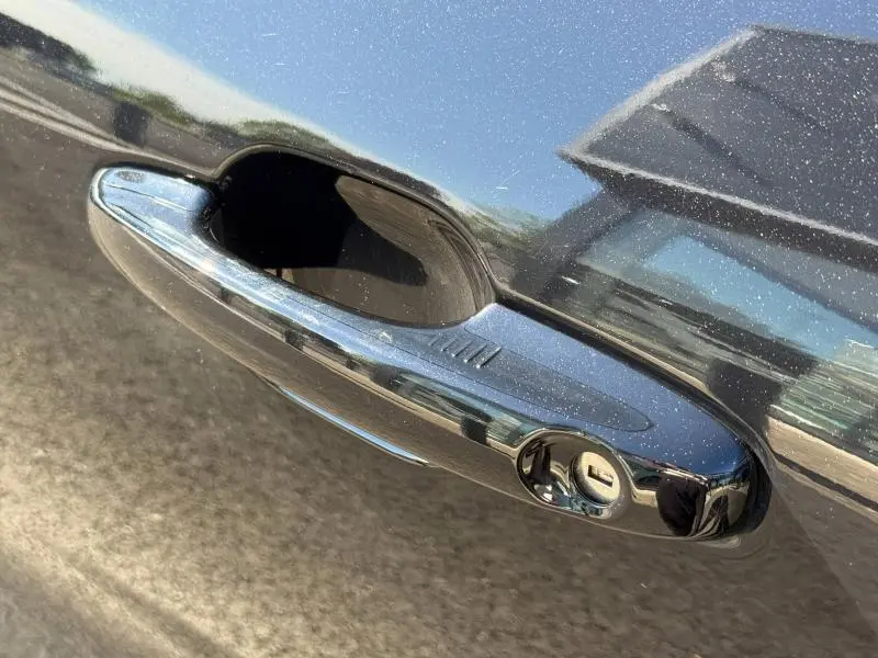 Gros plan sur la poignée de porte chromée du Ford Kuga noir Agate Métallisée, reflet de l’environnement visible.