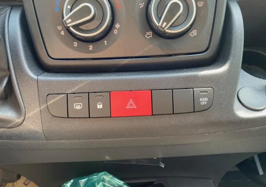 Vue rapprochée des commandes de climatisation et des boutons de sécurité sur le tableau de bord du Citroën Jumper blanc 2023.