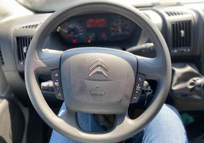 Vue rapprochée du volant noir du Citroën Jumper 2023 avec commandes intégrées et tableau de bord en arrière-plan.