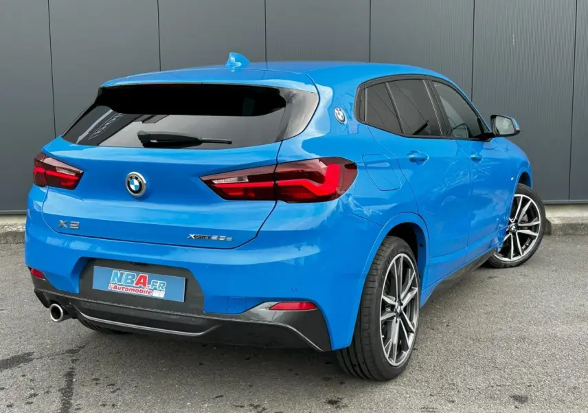 Vue 3/4 arrière droite d'un BMW X2 F39 xDrive 25e bleu Misano avec jantes alliage bicolores et hayon électrique.