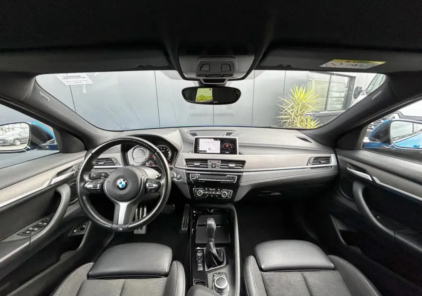 Vue intérieure frontale du BMW X2 F39 2021, tableau de bord noir avec volant M cuir et écran GPS central.