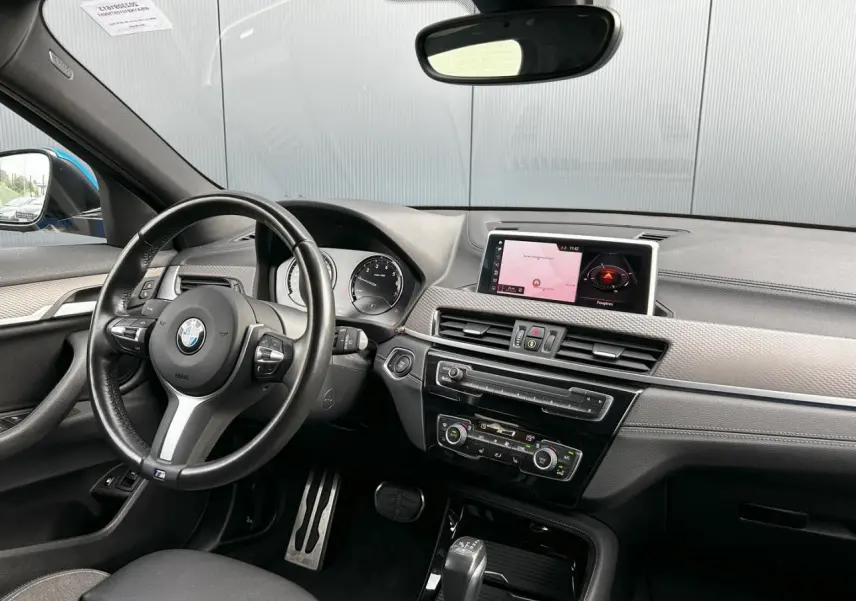 Intérieur BMW X2 F39 vu côté conducteur, volant cuir M, tableau de bord avec écran GPS et finitions grises anthracite.