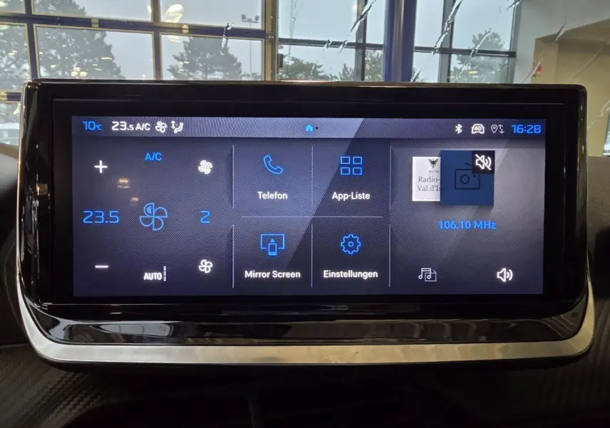 Écran tactile central du tableau de bord du Peugeot 208 1.2i Hybrid en intérieur, affichage des commandes climatisation et multimédia.