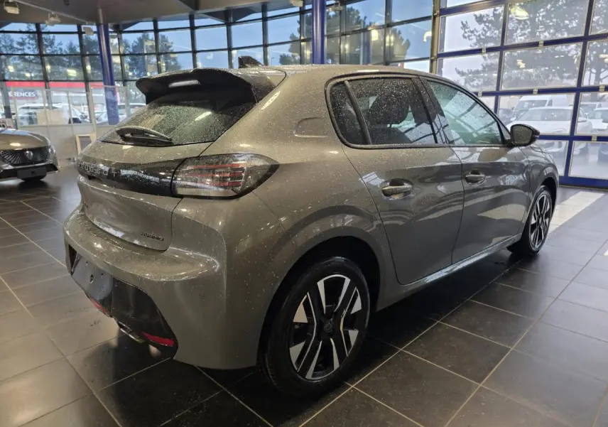 Peugeot 208 gris Selenium vue 3/4 arrière droit en intérieur, avec jantes alliage bi-tons et becquet noir brillant.
