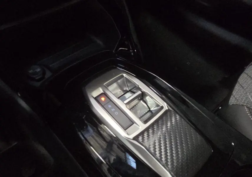 Gros plan sur la console centrale de la Peugeot 208 hybride 2025 avec levier de vitesses automatique et finition carbone.