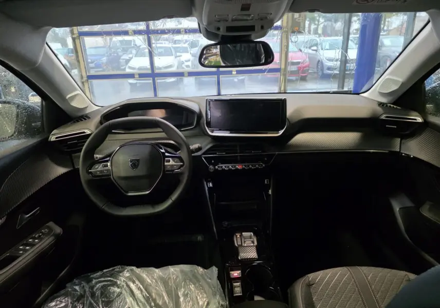 Vue intérieure avant du Peugeot 208 2025 avec tableau de bord noir, volant compact et écran tactile central.