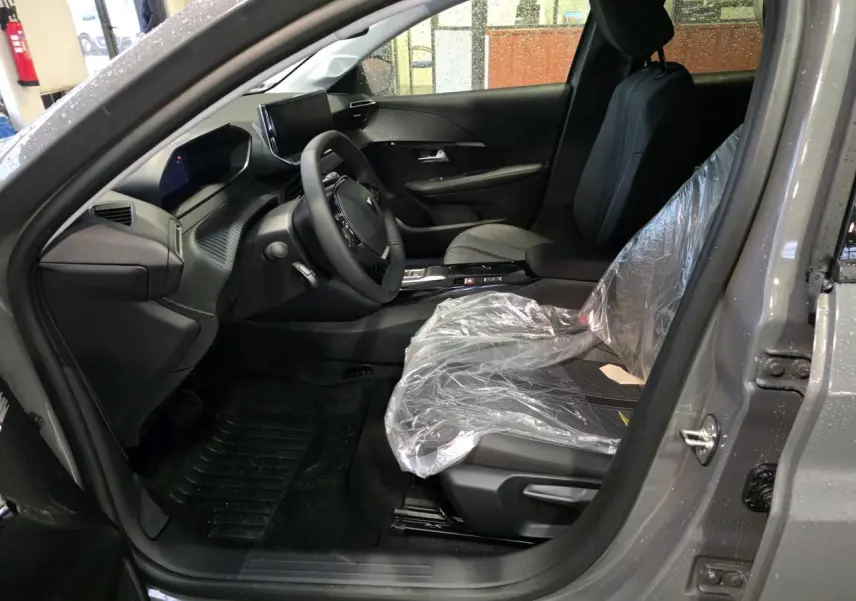 Vue intérieure côté conducteur de la Peugeot 208 gris selenium, montrant le tableau de bord et siège avant protégé.