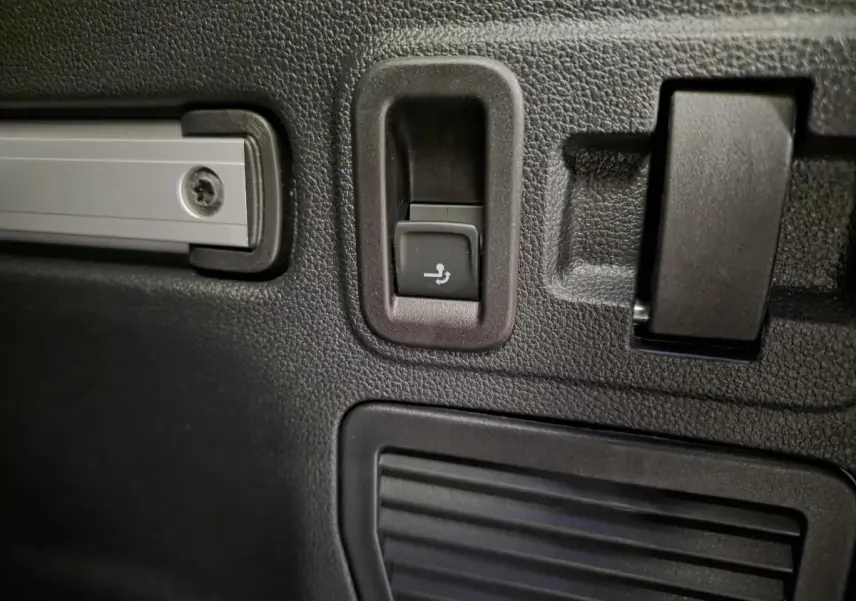 Détail du bouton de rabattement électrique des sièges arrière dans le coffre du Volkswagen Touran noir 2025.