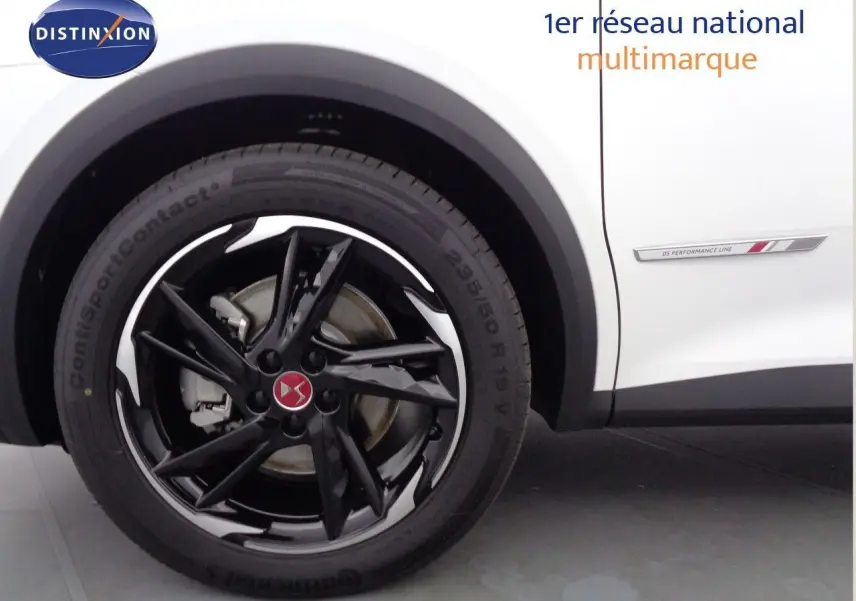 Gros plan sur la roue avant gauche noire brillante et la carrosserie blanche nacrée du DS7 Crossback E-TENSE 300CH PERF LINE +