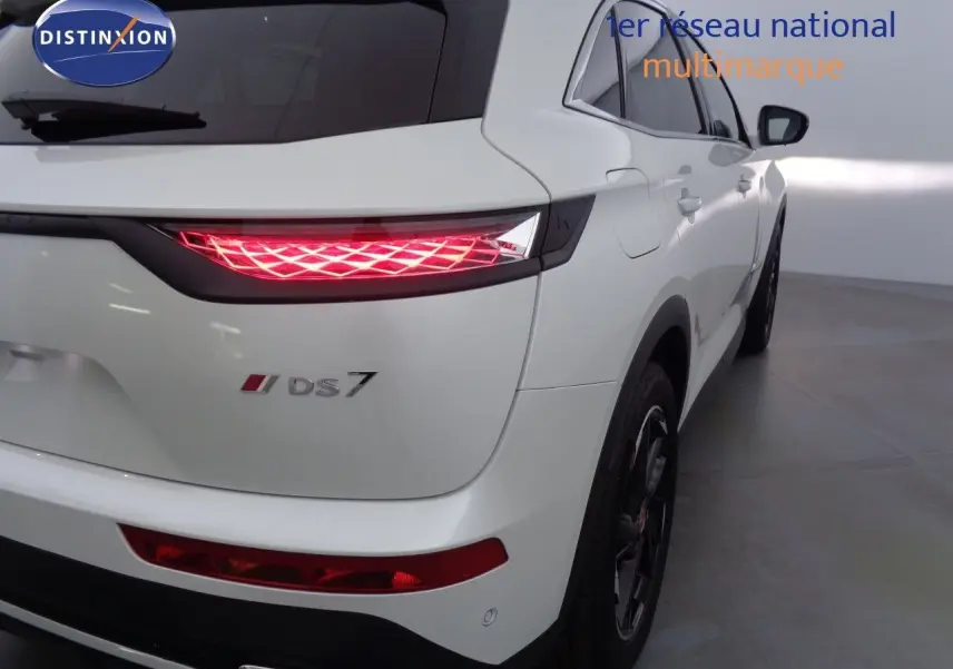 Vue 3/4 arrière droite du DS7 Crossback blanc nacré avec feux arrière LED allumés dans un intérieur lumineux.