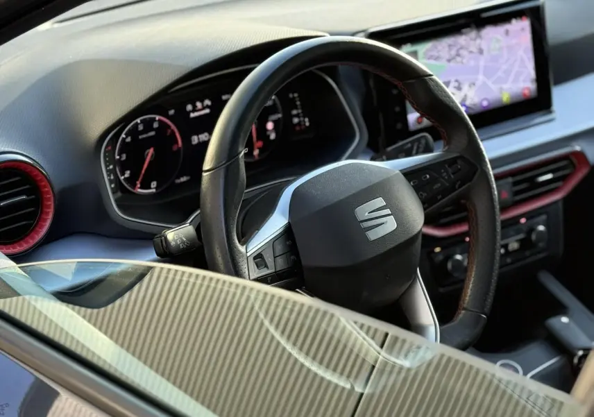 Vue rapprochée du volant noir avec logo SEAT et tableau de bord digital, intérieur souligné de touches rouges.