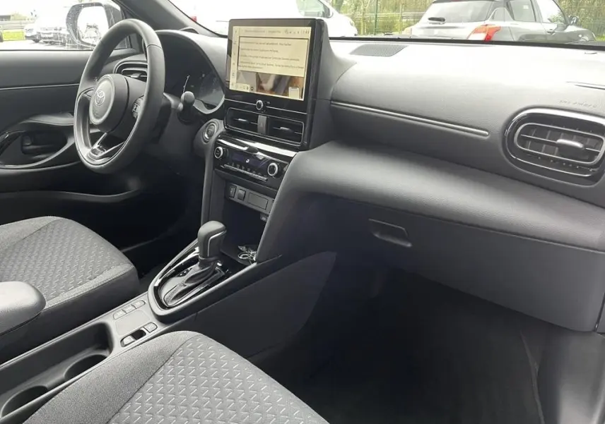 Intérieur avant droit de la Toyota Yaris Cross 2026 gris clair, volant cuir, écran tactile vertical et boîte auto visible.