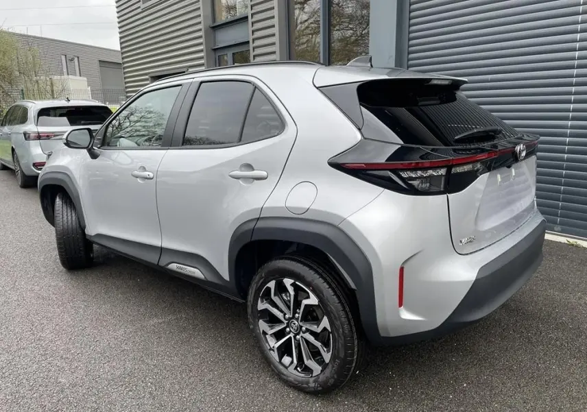 Vue 3/4 arrière droit d'une Toyota Yaris Cross gris clair avec jantes alliage et détails noirs sur le hayon.