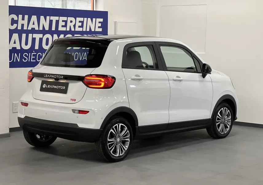 Vue 3/4 arrière droite d'une Dacia Spring blanche électrique LEAP MOTOR T03 avec toit noir et feux arrière allumés.