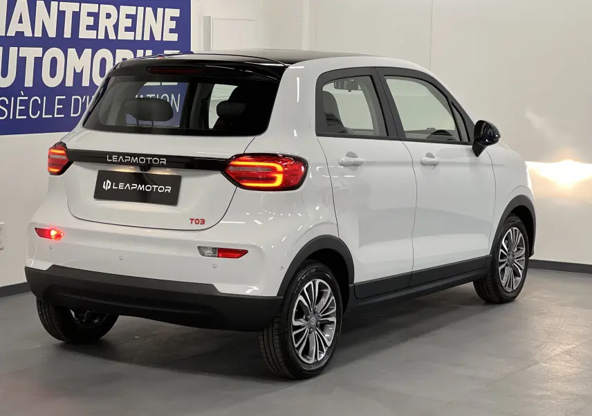 Vue 3/4 arrière droite d'une Dacia Spring blanche électrique avec feux arrière allumés et toit noir contrastant.