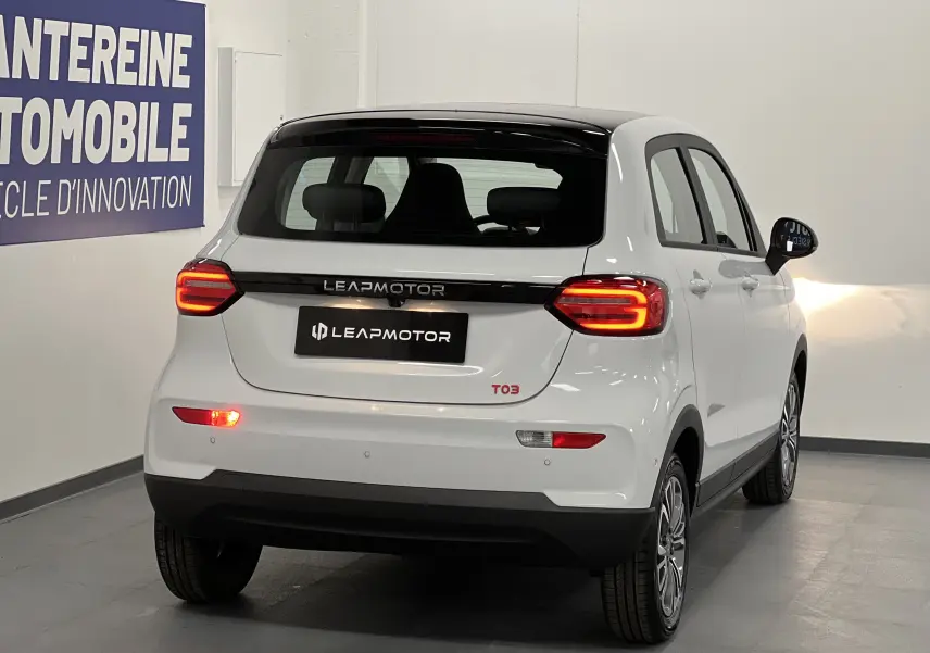 Vue 3/4 arrière droite d'une Dacia Spring blanche électrique avec feux arrière allumés et logo LEAPMOTOR sur le hayon.