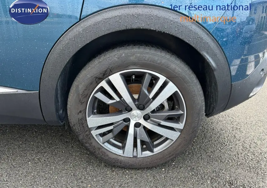 Gros plan sur la roue avant droite d'un Peugeot 3008 bleu Célèbes avec jante alliage bicolore mouillée.