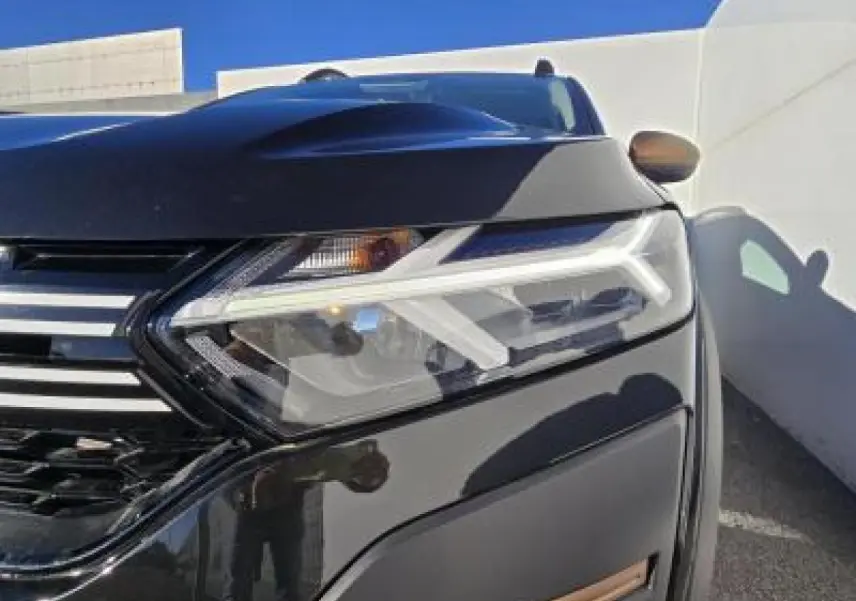 Gros plan sur le phare avant droit d'une Dacia Sandero Stepway 2025 noir nacré avec calandre chromée.