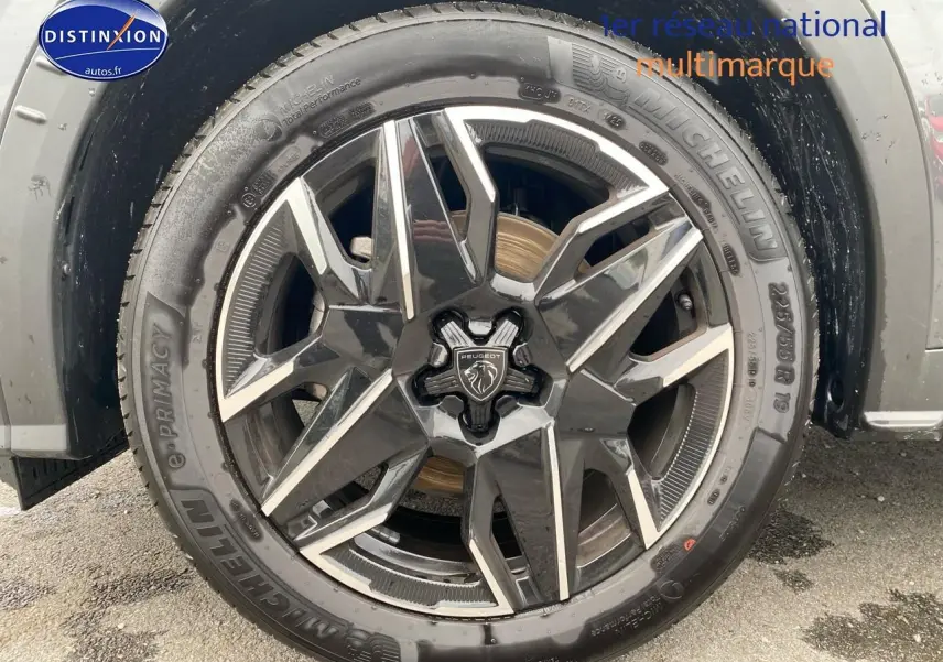 Gros plan sur la jante alu noire et argentée d’un Peugeot 5008 gris titane, mettant en valeur le logo central lion.