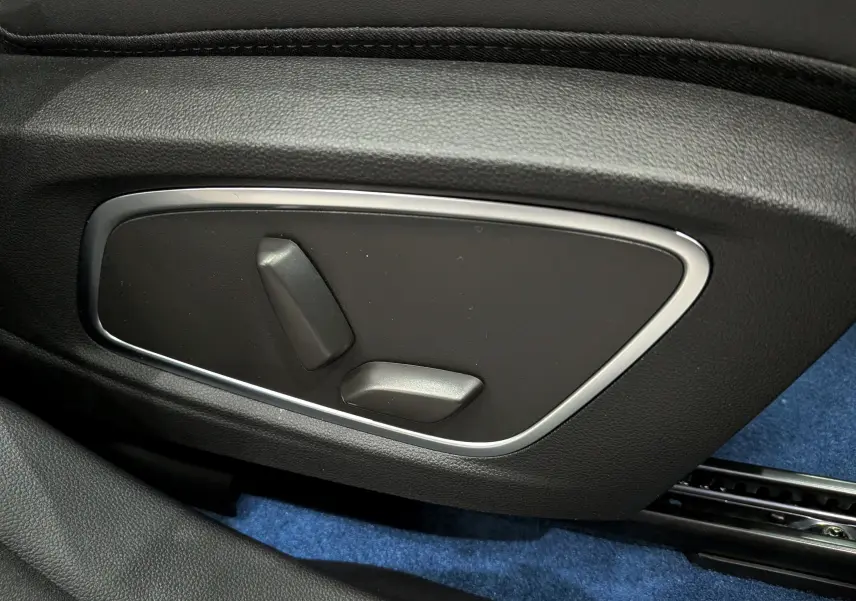 Détail des commandes de réglage électrique du siège côté gauche, intérieur noir avec moquette bleue.