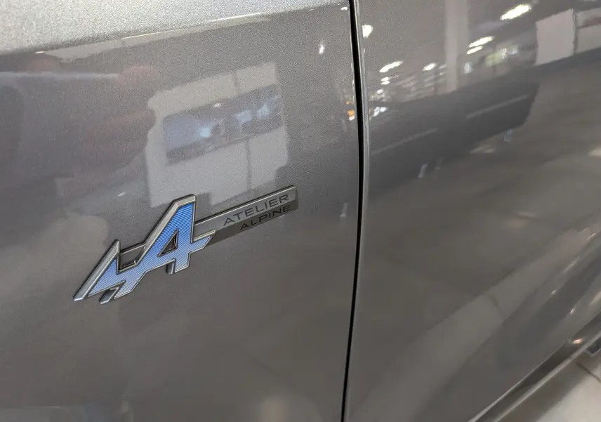 Gros plan sur l'écusson Atelier Alpine bleu sur la porte gris schiste du Renault Rafale hyper hybrid 2026.