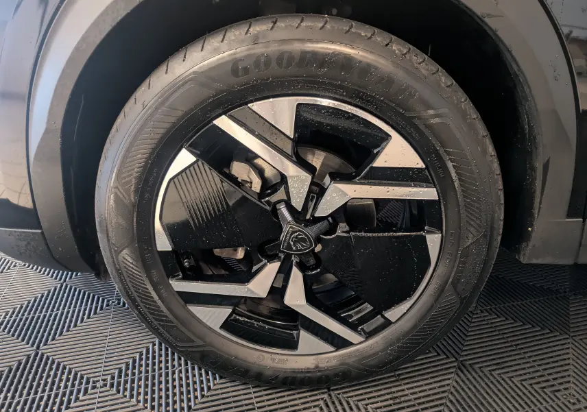 Gros plan sur la jante alliage 17'' noire et argentée d'un Peugeot 2008 noir Perla avec logo Peugeot central.