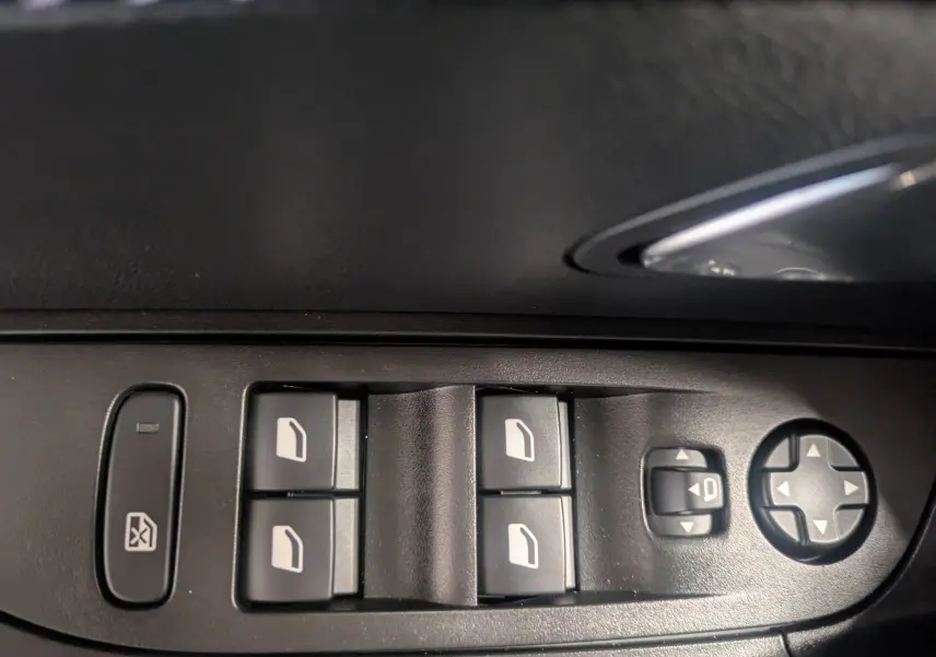 Gros plan sur les commandes de lève-vitres et réglage des rétroviseurs côté conducteur d'une Peugeot 2008 noire.