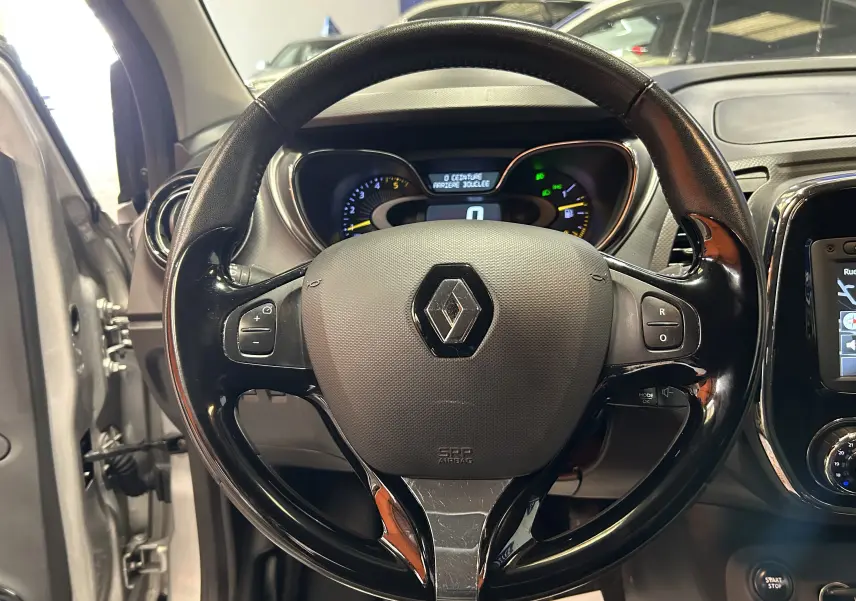 Volant noir brillant avec logo Renault au centre, tableau de bord et écran GPS visibles dans un Renault Captur gris 2015.
