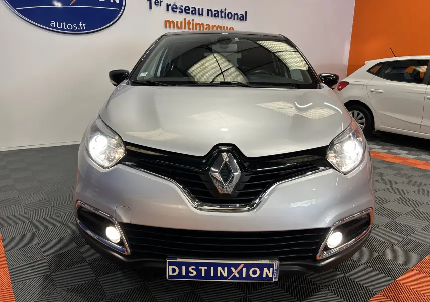 Vue frontale d'un Renault Captur gris avec phares et feux antibrouillard allumés dans un showroom.