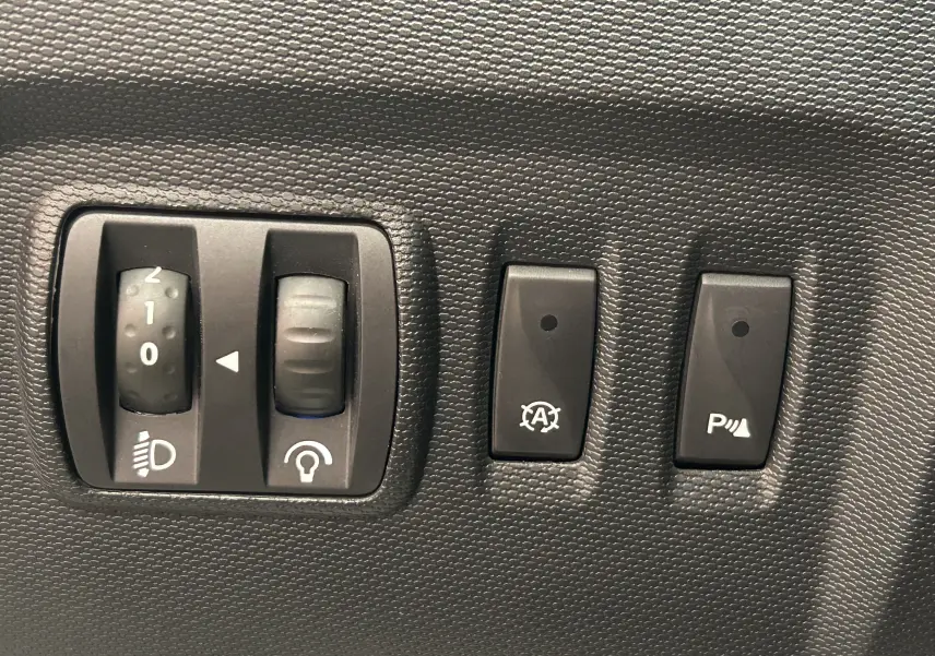 Gros plan sur les commandes de réglage des phares et activation du radar de recul dans un Renault Captur gris 2015.