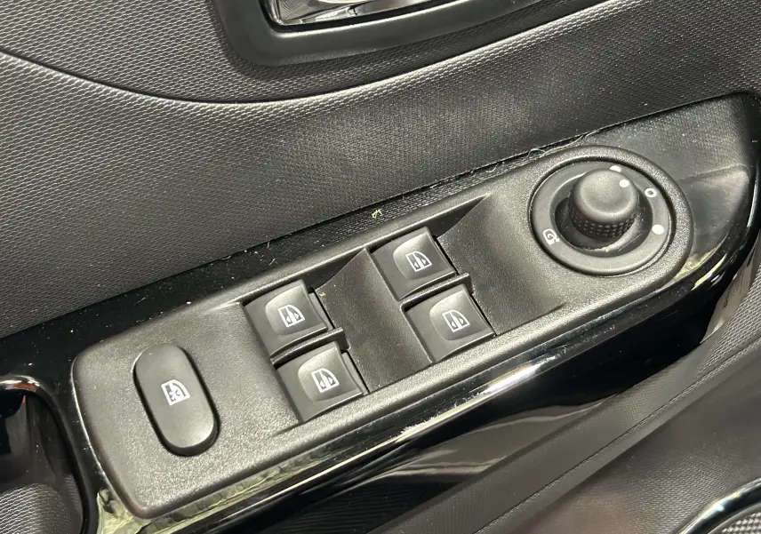 Gros plan sur les commandes de lève-vitres et réglage des rétroviseurs côté conducteur d’un Renault Captur gris.