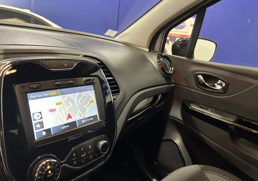 Vue intérieure côté passager du tableau de bord du Renault Captur gris avec écran GPS allumé et commandes de climatisation.