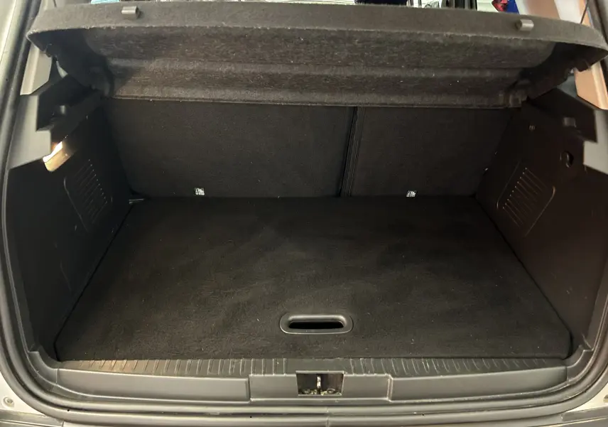 Coffre ouvert d'un Renault Captur gris 2015, vue arrière montrant l'espace de chargement vide et la moquette noire.