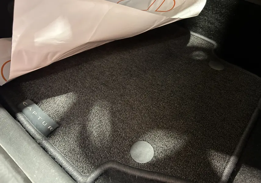 Tapis de sol noir avec étiquette Captur dans l'habitacle d'un Renault Captur gris, vue en gros plan intérieur côté passager.