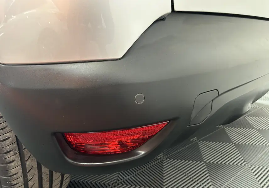 Gros plan sur le pare-chocs arrière gris du Renault Captur 2015, avec feu rouge et capteur de recul visible côté droit.