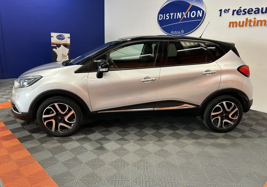 Profil côté gauche d'un Renault Captur gris 2015 avec toit noir, jantes alliage et détails chromés en intérieur showroom.