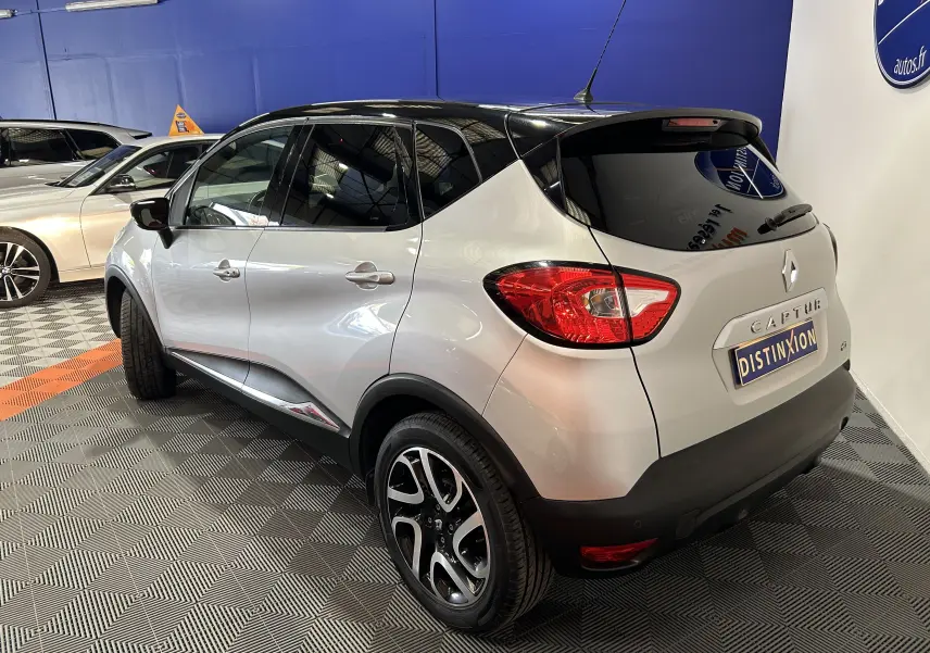 Vue 3/4 arrière droite d'un Renault Captur gris 2015 avec toit noir et jantes alliage distinctives.