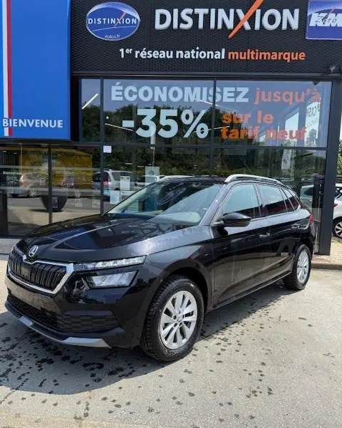 Vue 3/4 avant droite d'un Skoda Kamiq noir 2024 garé devant une vitrine de concession multimarque.
