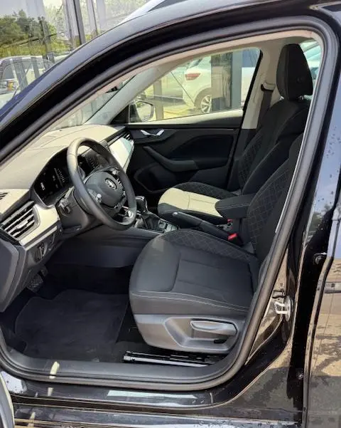 Vue intérieure côté conducteur du Skoda Kamiq noir 2024, montrant sièges tissu noir et tableau de bord moderne avec écran tactile.
