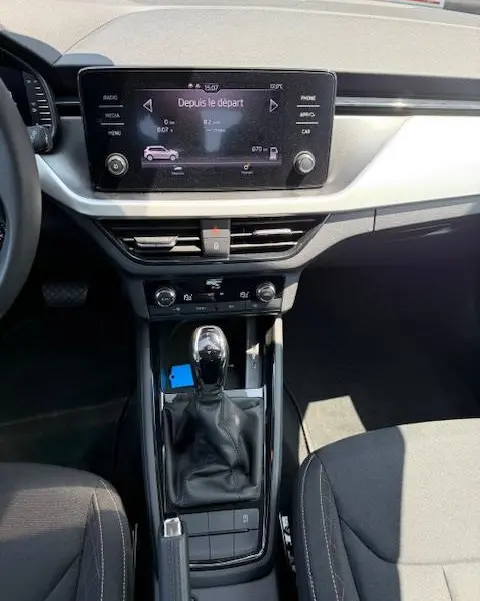 Vue intérieure centrée sur la console centrale et l'écran tactile du Skoda Kamiq noir, avec levier de vitesse automatique.
